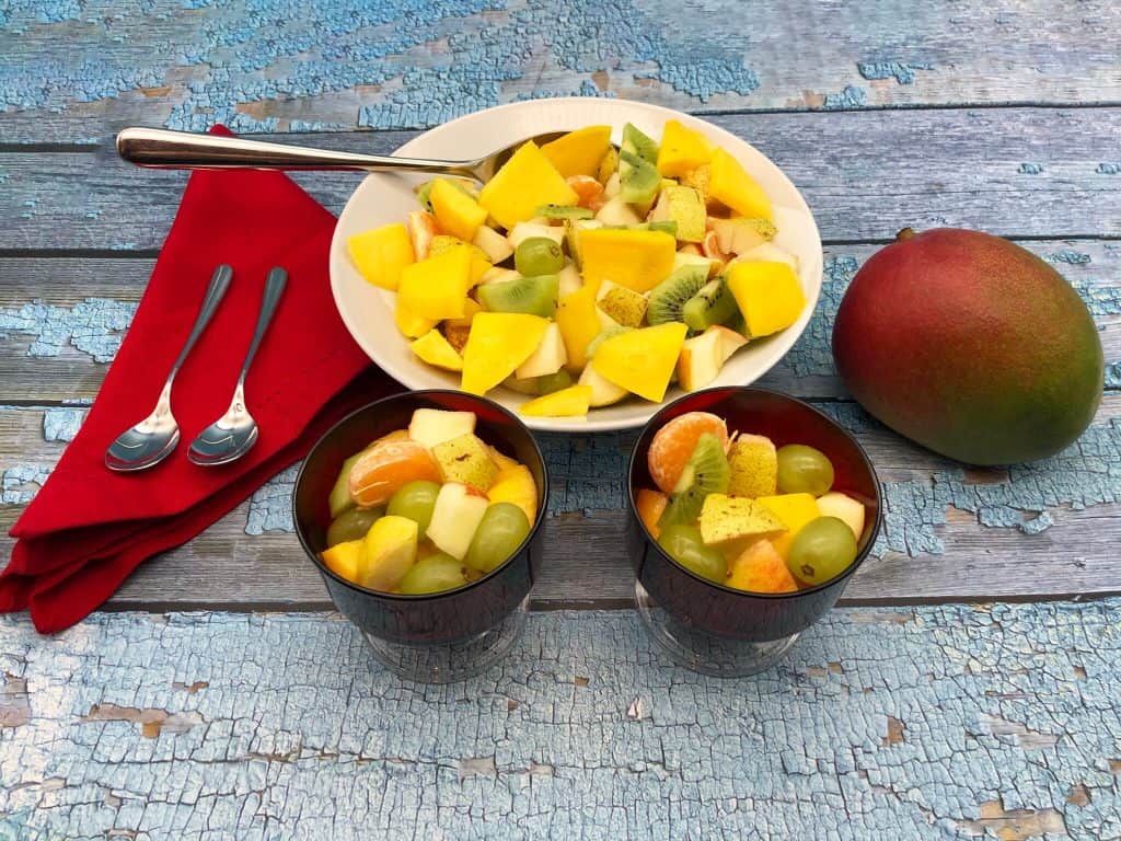 A bowl full of healthy fresh fruit salad chopped and a whole mango