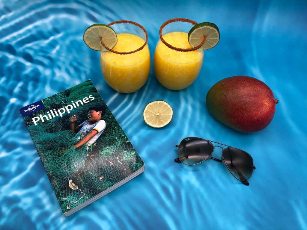 Holiday mocktails with mango, lime, sunglasses and travel book