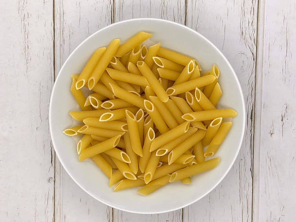 Dried penne pasta in a white bowl