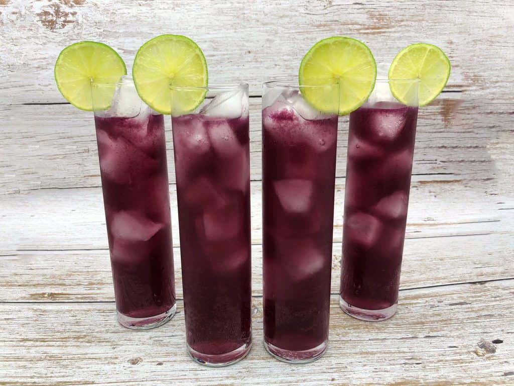 Four purple rain cocktails with lime