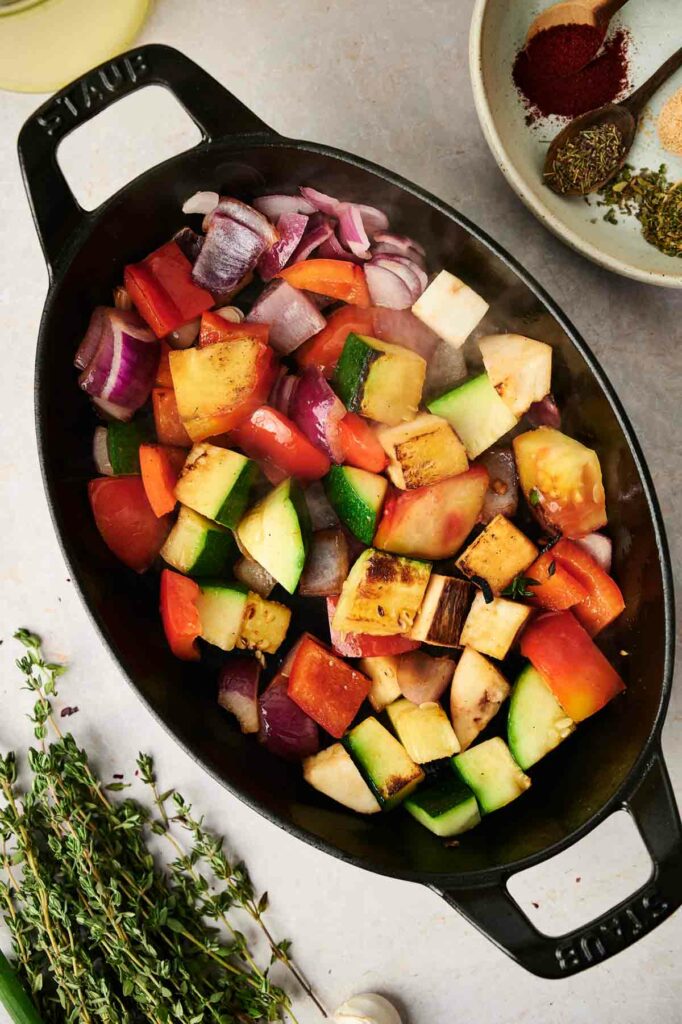 A mouthwatering ratatouille recipe prepared in a cast iron skillet with an array of vibrant vegetables and aromatic herbs.