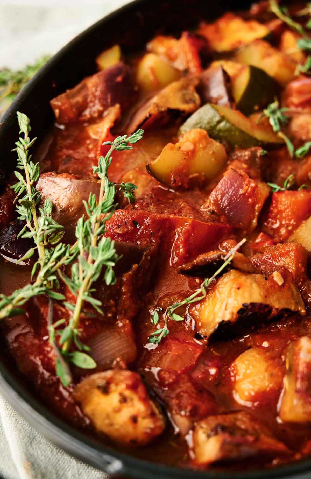 A ratatouille recipe showcasing a skillet full of meat and vegetables with sprigs of thyme.