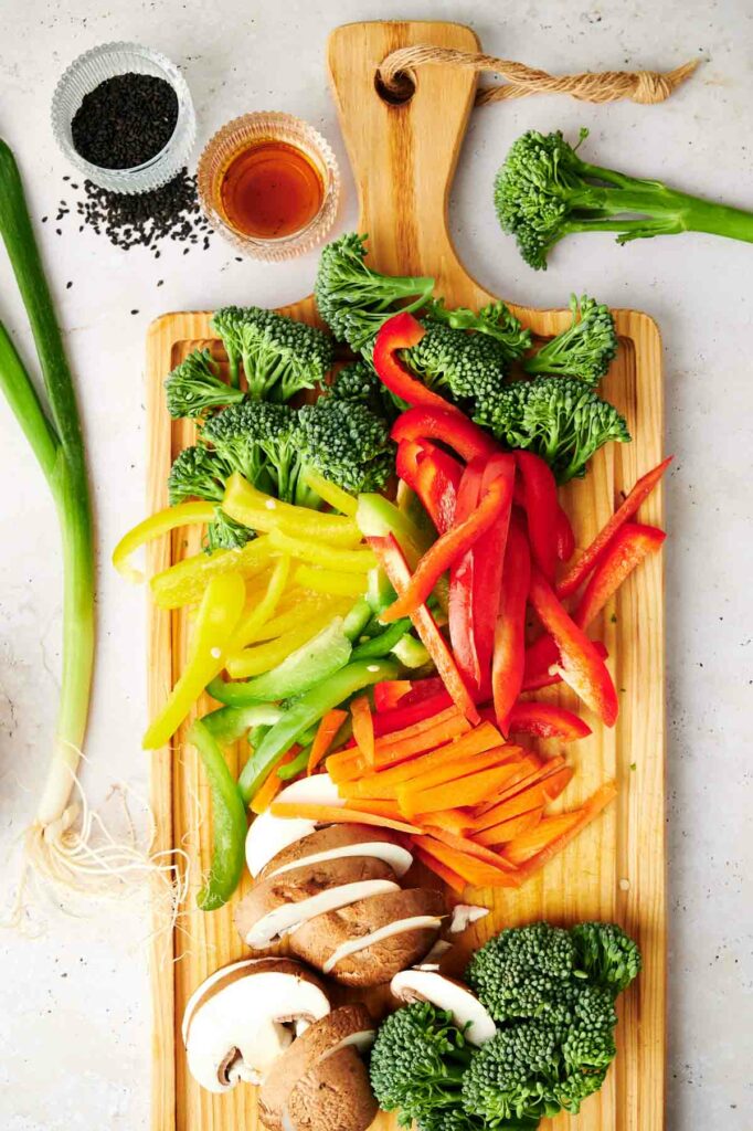 A wooden cutting board with sliced vegetables for a vegetable stir fry.