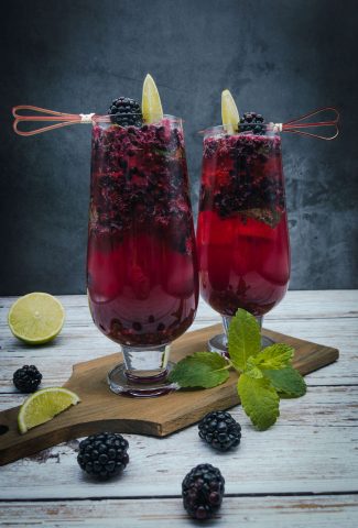 Two blackberry mojitos with fresh blackberries, lime wedges and a sprig of mint