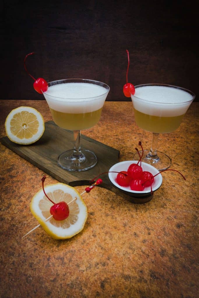 Two whiskey sour mocktails with cherries and lemon