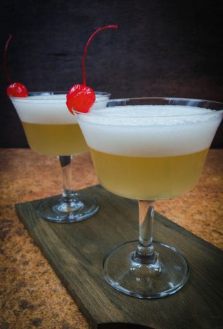 Two beautiful whiskey sour mocktails with a maraschino cherry garnish