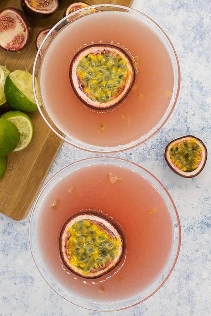 Beautiful passion fruit daiquiri drink with floating passion fruits as garnish, with a board of lime and passion fruit skins.