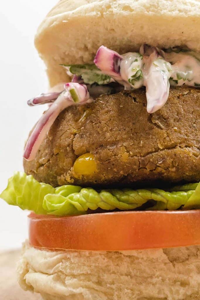 Close up of golden brown vegan chickpea burger ready to eat with red cabbage slaw oozing out