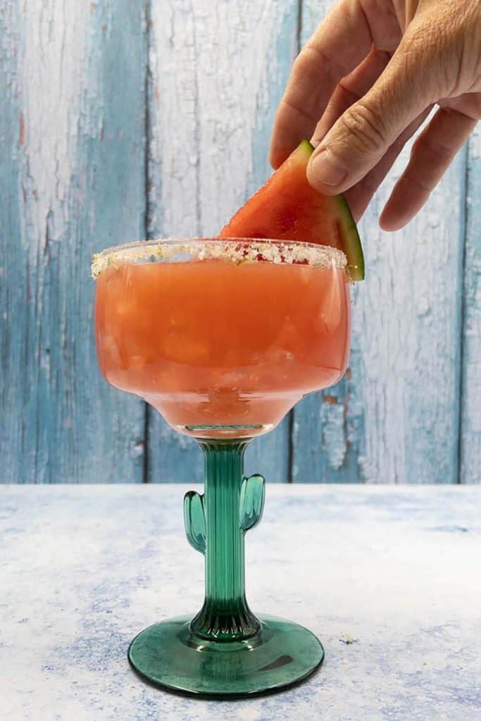 Placing garnish on watermelon margarita made with tequila in cactus margarita glass.