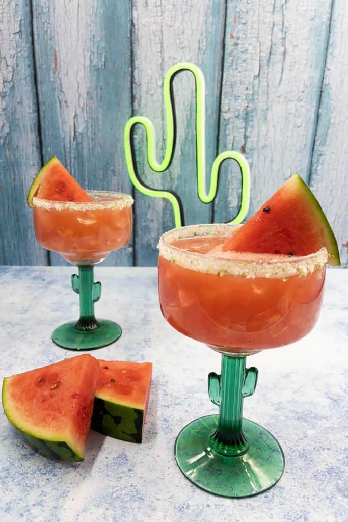 Two watermelon margaritas made with tequila with neon cactus in the background.