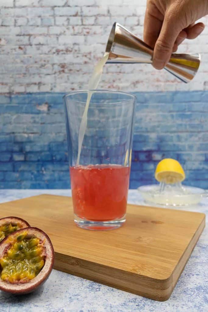 Adding lemon juice into passion fruit mixture in a cocktail shaker.