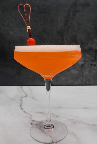 Aperol sour cocktail in a coupe cocktail glass with a maraschino cherry garnish.