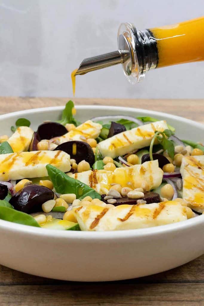 A drizzle of salad dressing being poured over grilled halloumi salad.