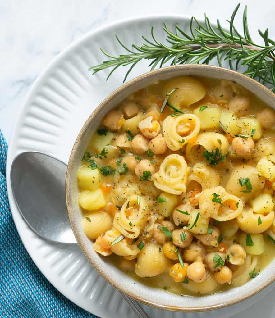 Tasty bowl of Italian pasta and chickpeas with a sprig of rosemary.