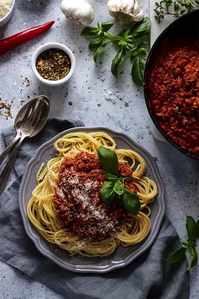 A delicious plate of vegan spaghetti bolognese with a sprig of basil on top.