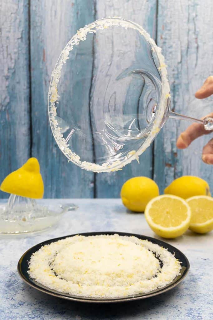 A margarita glass with a salt rim, fresh lemons and salt with lemon zest