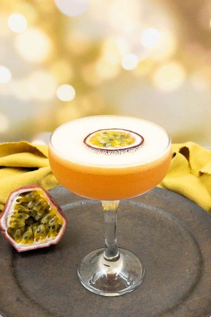 Freshly made pornstar martini with a frothy top and a passion fruit floating, a shot of prosecco and passion fruits