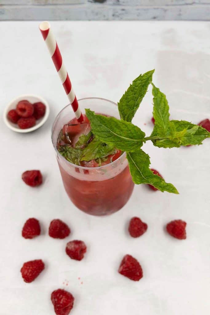 Overhead shot of a homemade raspberry mojito cocktail with fresh mint and a striped straw.