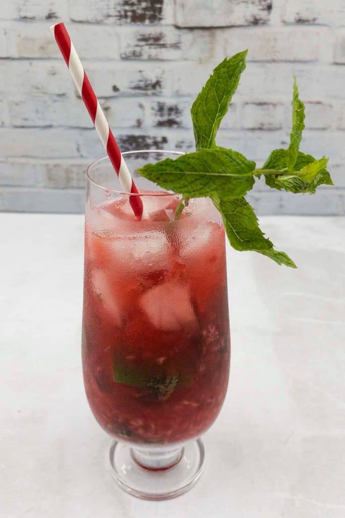 A summer raspberry mojito drink with a straw and fresh mint garnish.