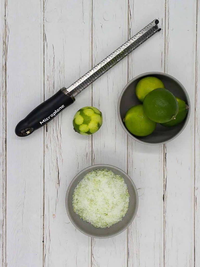 A lime zester, fresh limes and a bowl of sweet lime sugar.