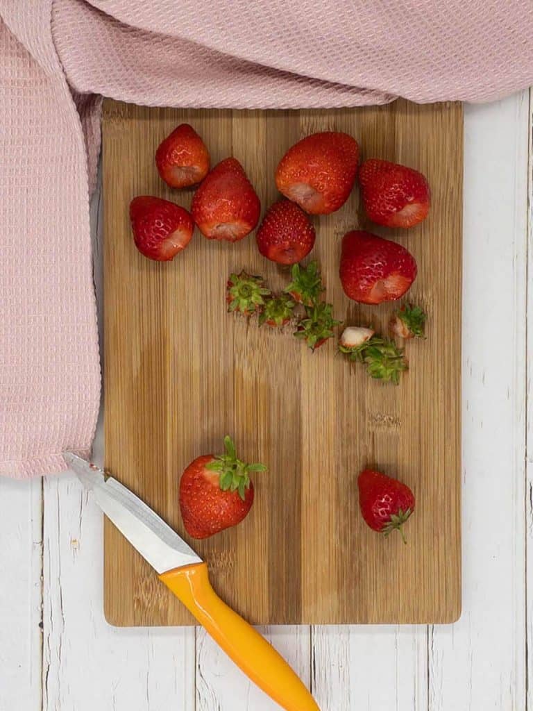 Strawberries being hulled on a cutting board.