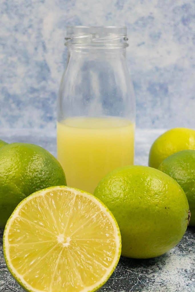 Freshly squeezed lime juice in a bottle with limes surrounding it and one cut in half.