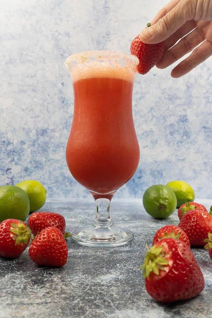 Placing the garnish on a virgin strawberry daiquiri drink with a sweet fresh strawberry.