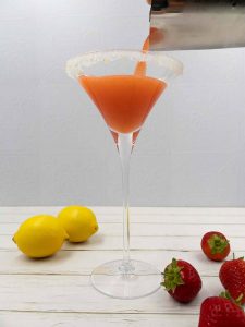 Pouring a strawberry martini into a martini glass.