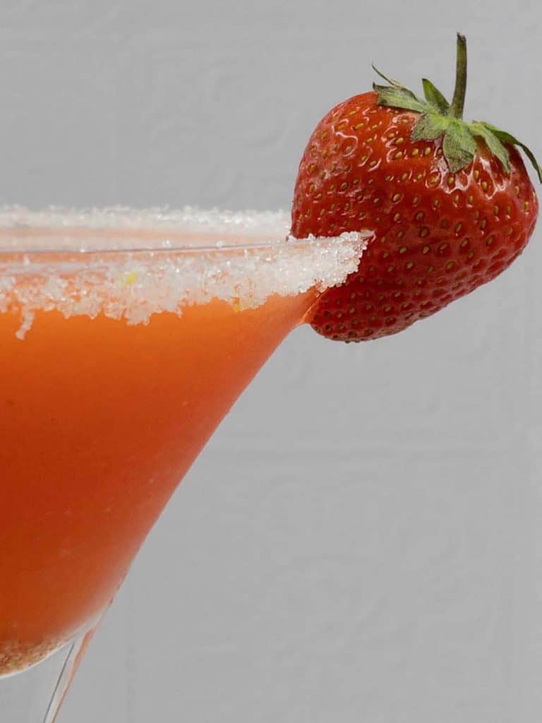 A strawberry garnish on a homemade strawberry martini with a sugared rim.