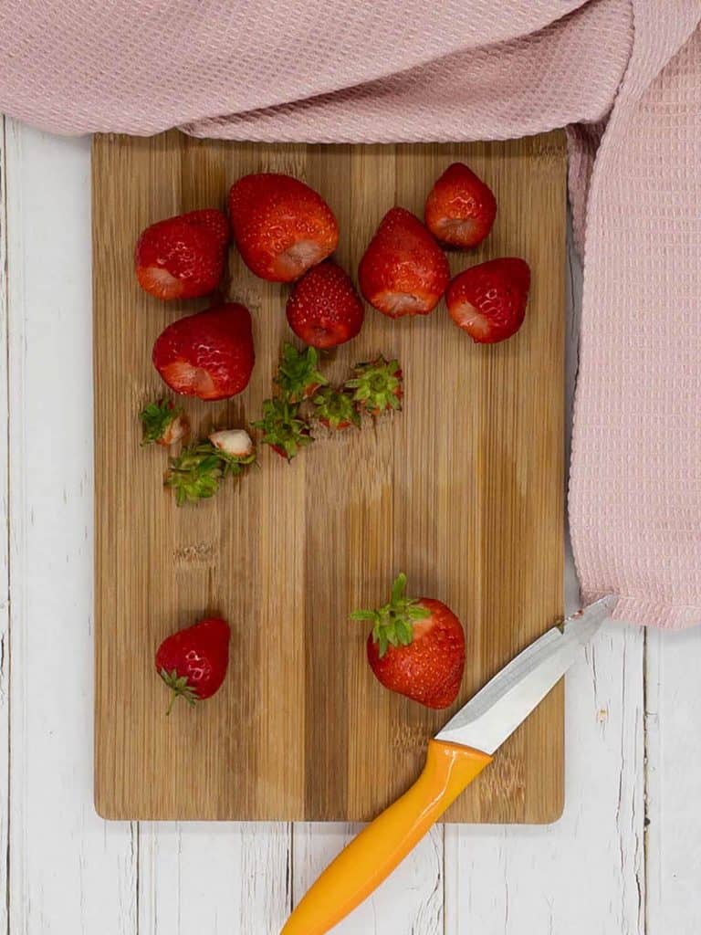 Hulling fresh strawberries on a chopping boardd.