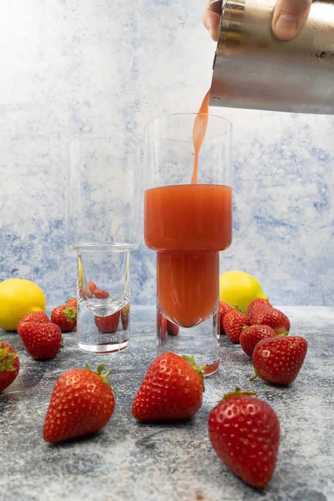 Pouring vodka strawberry lemonade cocktail drinks into glasses.