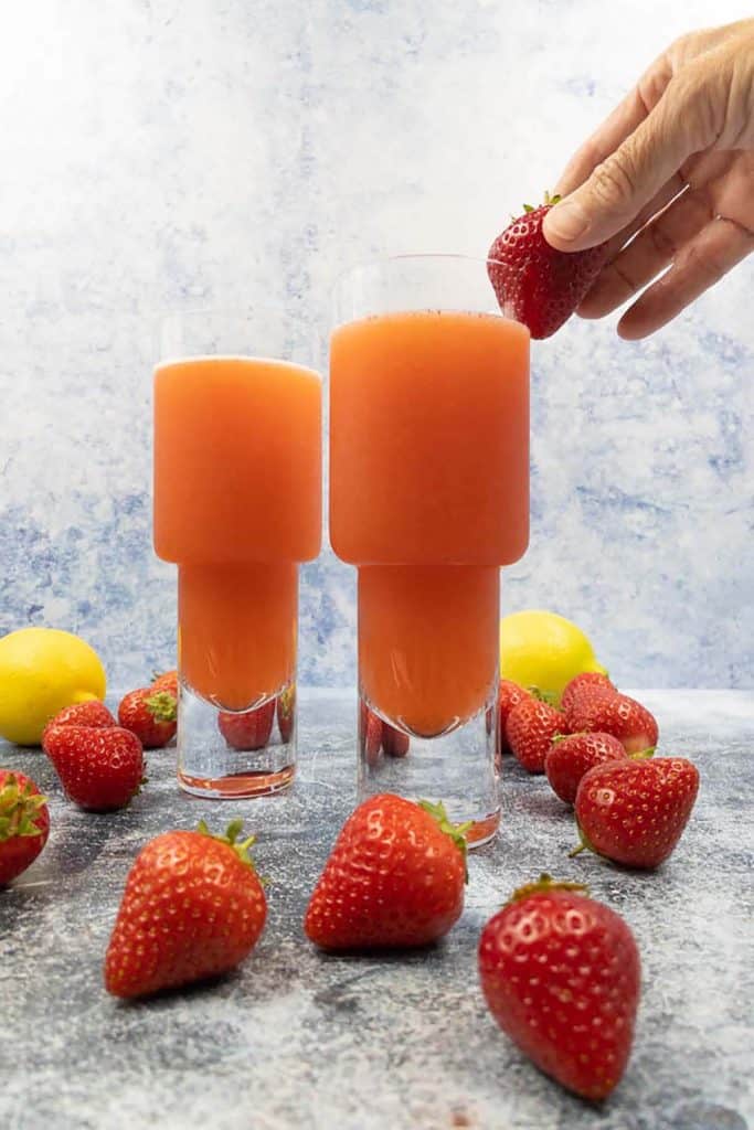 Placing a strawberry garnish on a vodka strawberry lemonade drink, with strawberries and fresh lemon.