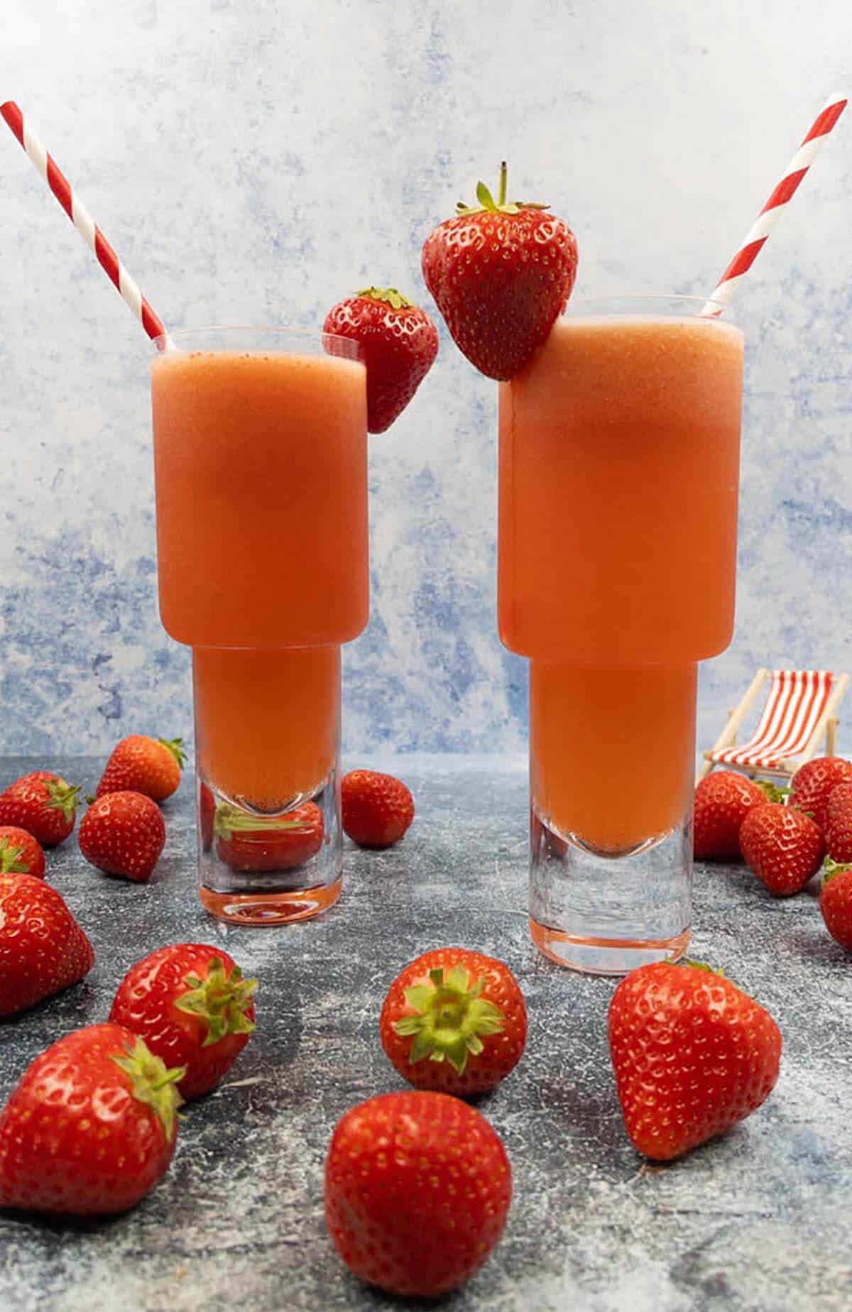Two strawberry lemonade vodka cocktails with fresh strawberries, striped straws and a deck chair.