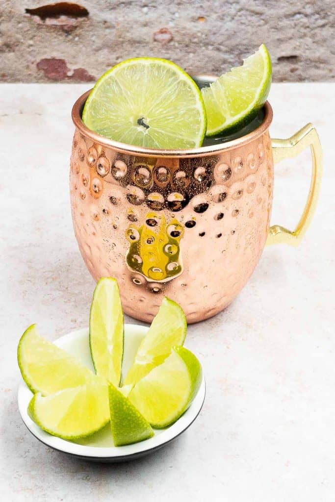 A homemade mule cocktail drink, in a copper mug, with lime wedges and wheels.