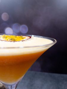 Close up of a homemade pornstar martini gin cocktail with a fresh passionfruit garnish floating on top.