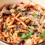 A pot of Pasta alla Norma with penne, rich tomato sauce, eggplant slices, grated cheese, herbs, and fresh basil leaves.