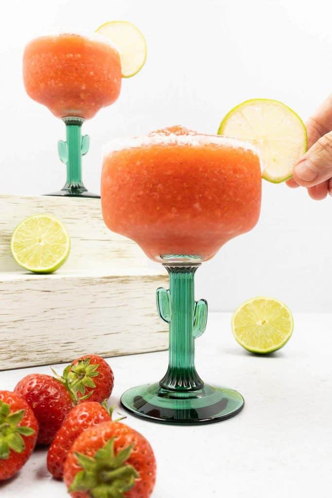 Placing a lime slice on a frozen strawberry margarita.