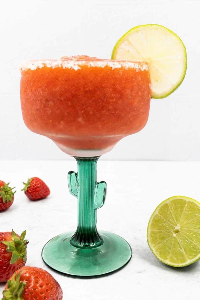 Delicious homemade frozen strawberry margarita recipe, with a slated rim and lime slice garnish.