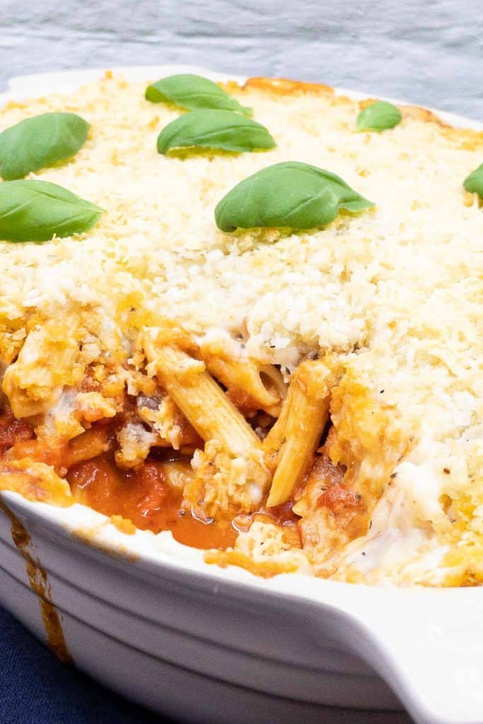 A baking dish of pasta al forno with a portion removed revealing the penne pasta and cheesy tomato filling.
