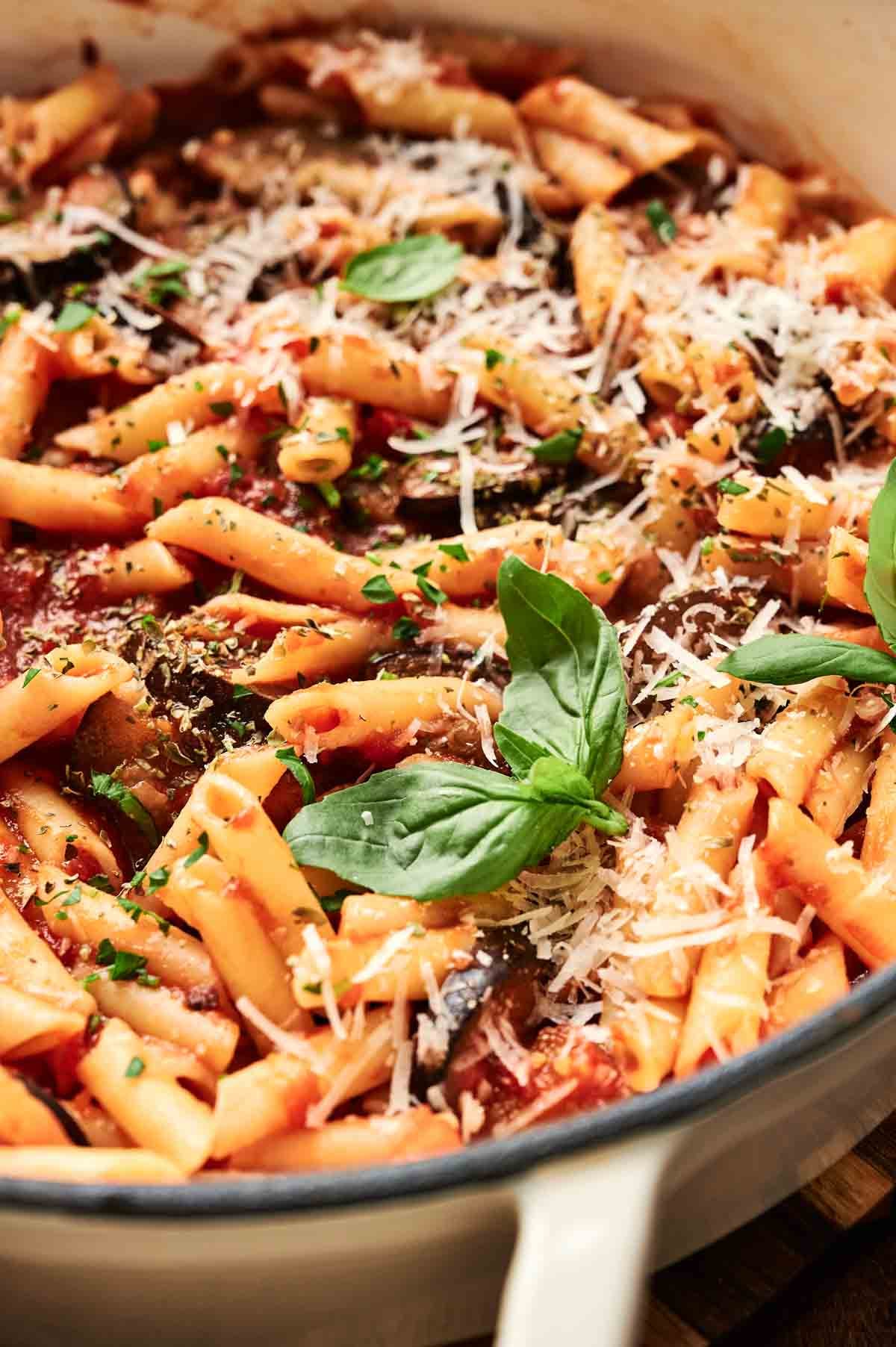 Pasta alla Norma with tomato sauce, mushrooms, and grated cheese, garnished with fresh basil in a white dish.