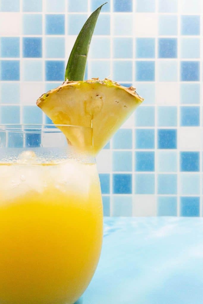 Close up of a pineapple tequila cocktail with a fresh pineapple wedge and leaf as garnish.