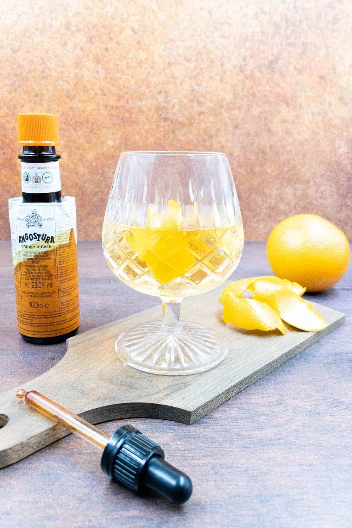 A tequila old fashioned with ice cube and orange peel, angostura bitters by the side.