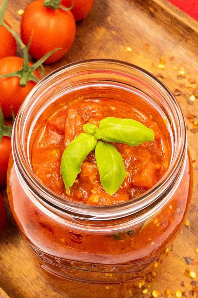 A jar of delicious arrabbiata sauce made from scratch with basil leaves and tomatoes.