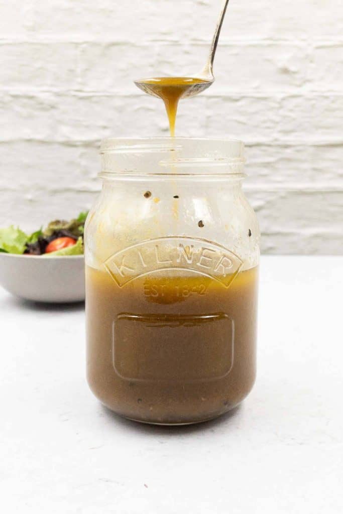 Freshly made balsamic vinaigrette dressing in mason jar with a spoon with vinaigrette flowing over it.