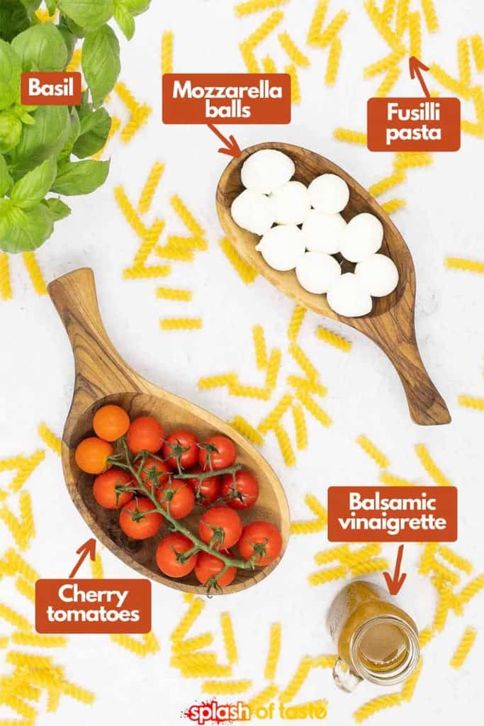 Ingredients for making a Caprese pasta salad from scratch, fresh basil, mozzarella balls, fusilli pasta, balsamic vinaigrette and cherry tomatoes.