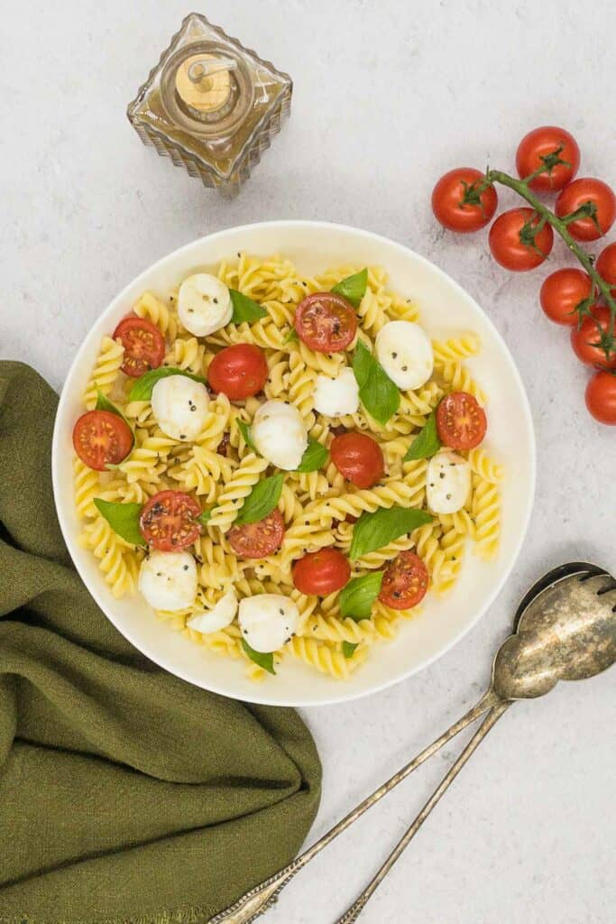 A bowl of homemade delicious Caprese pasta salad with salad servers and balsamic vinaigrette dressing.
