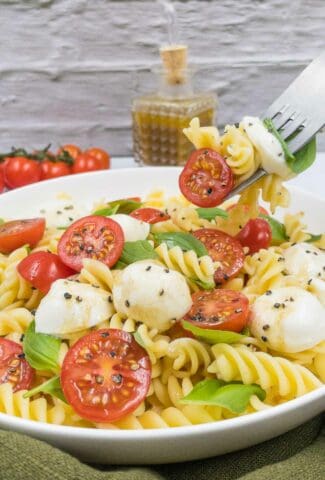 Homemade Caprese pasta salad with cherry tomatoes, mozzarella balls, basil and fusilli pasta.