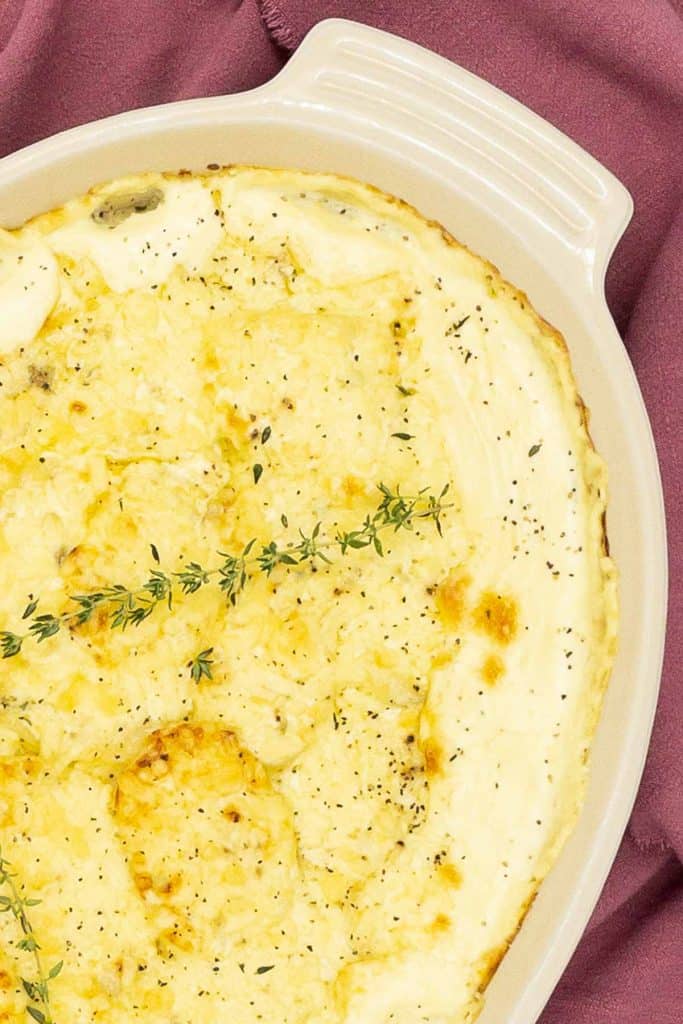Close up of dauphinoise potatoes with a golden brown cheese topping and a sprig of fresh thyme.
