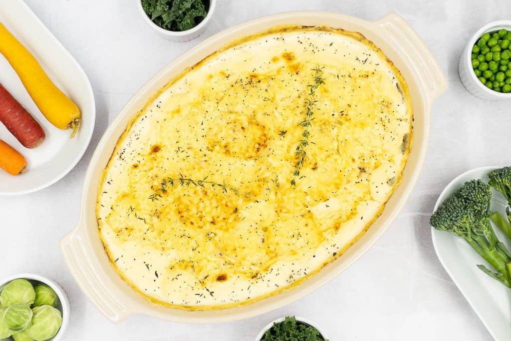 Potatoes dauphinoise with a delicious golden bubbly and golden brown cheese topping in a baking dish with seasonal vegetables.