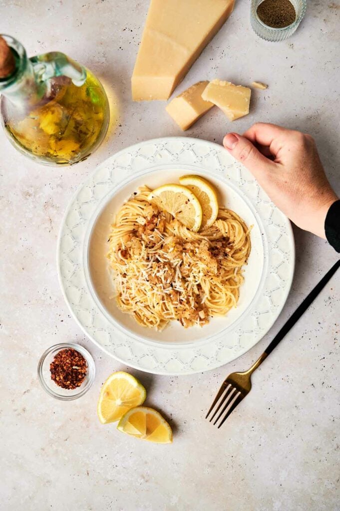 A hand holding a plate of lemon pasta.